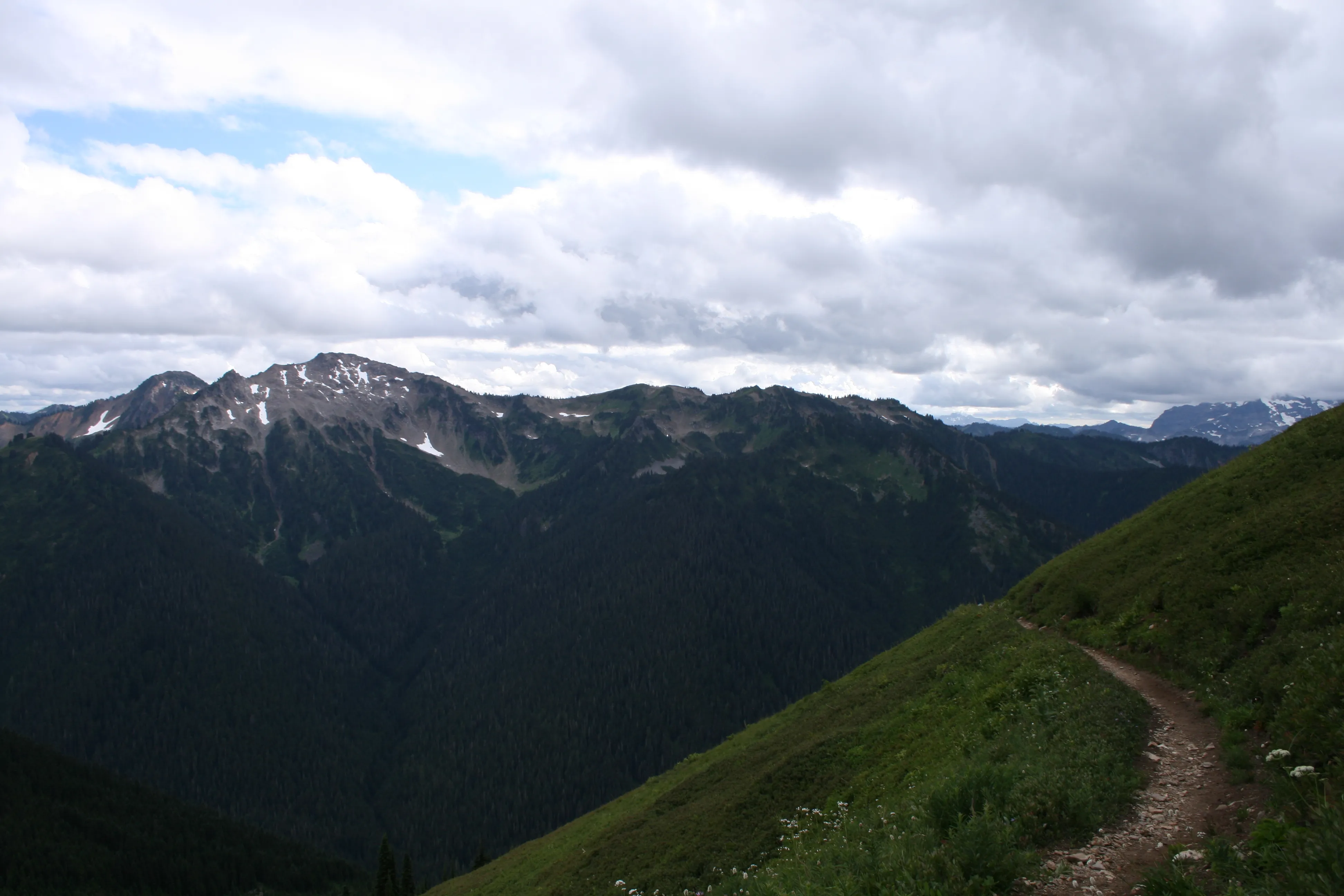 Single-track trail winding through the mountains under moody, cloudy skies on the approach