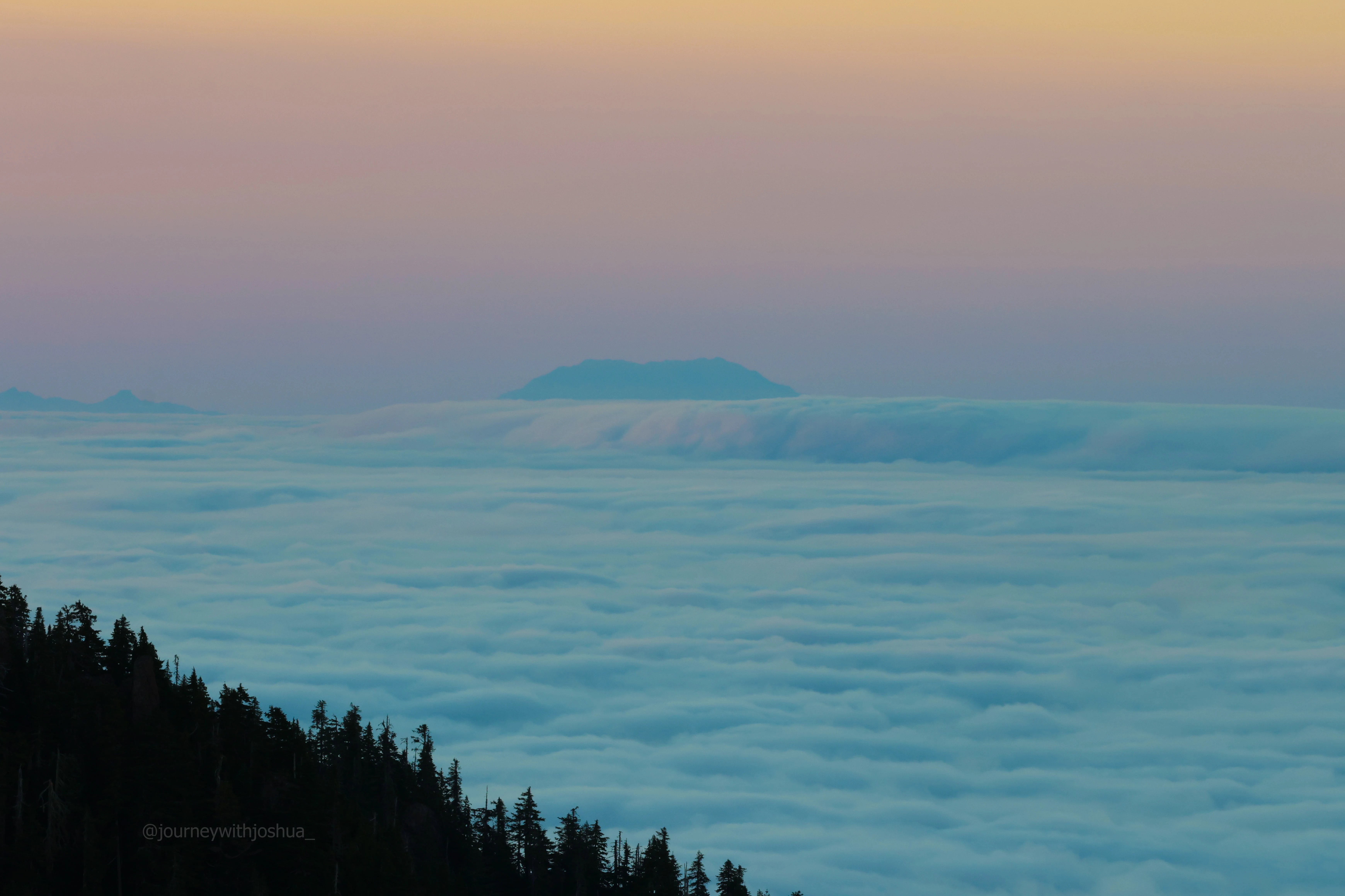 Mount St. Helens hiding just behind the cloud layer as seen from the Olympic Range at sunrise.