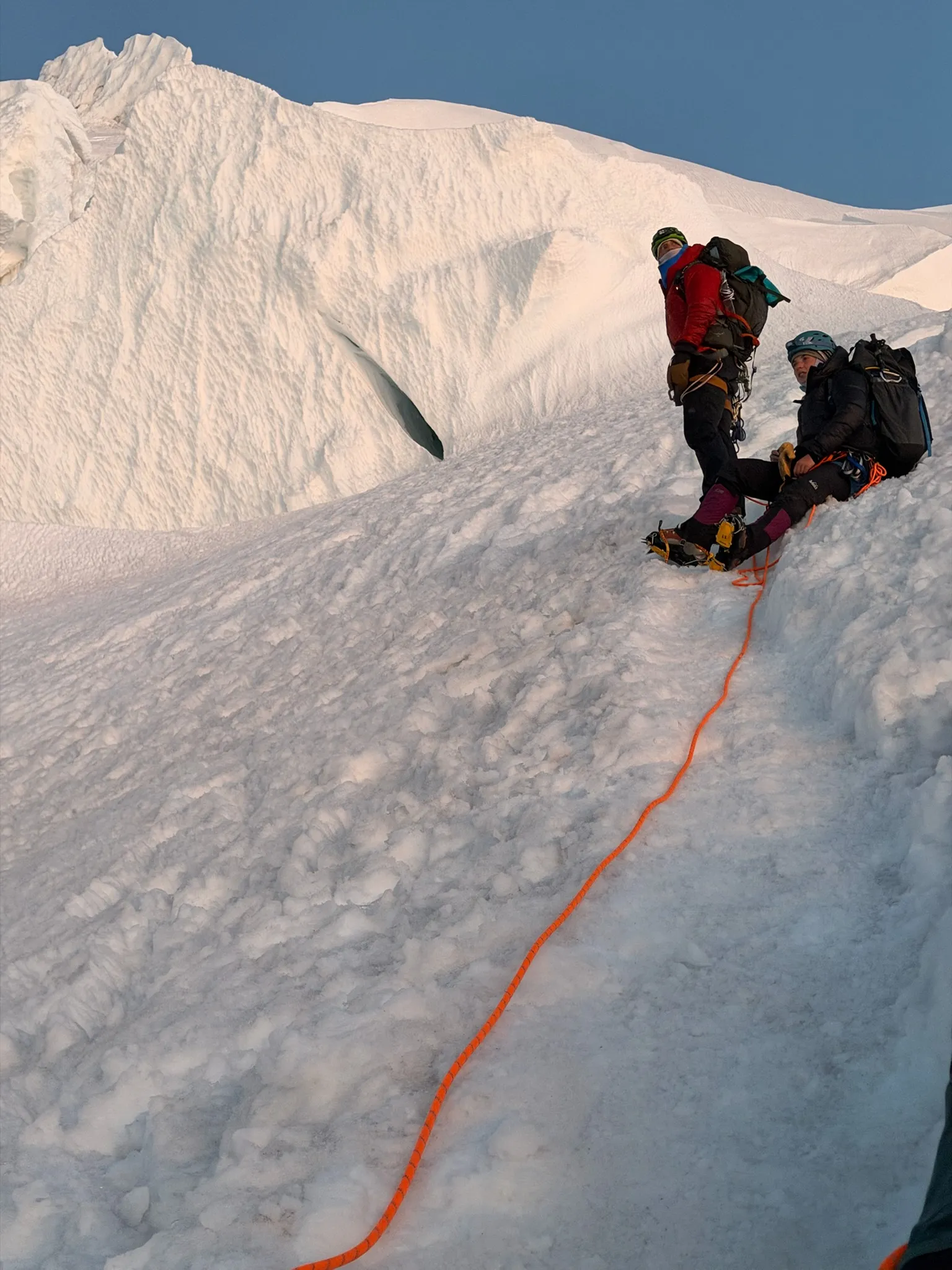 A quick rest below a towering serac on steep, icy terrain